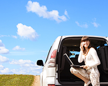 Woman stands outside of her van and uses her phone and lap top