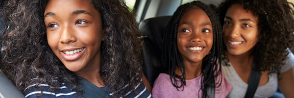 Mother and two children smile and look out the backseat window of a vehicle.