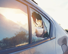 A parked dark sedan features a shattered second row window.