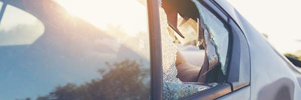 A parked dark sedan features a shattered second row window.