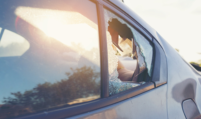 A parked dark sedan features a shattered second row window.