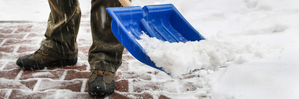 A person shovels snow off a brick path with a blue shovel.