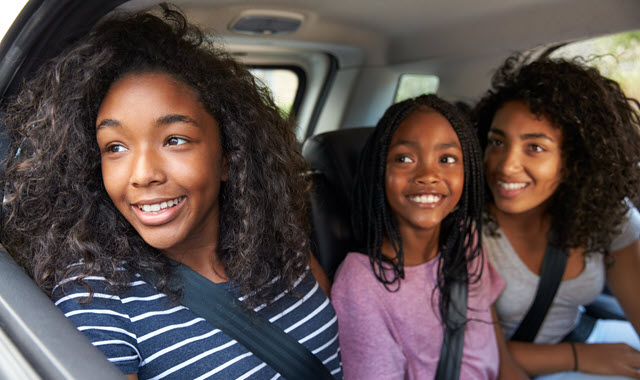 Kids in back seat smiling out the window of moving car