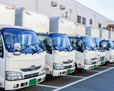 White trucks are parked in a line behind a distribution building.