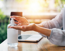 Woman uses hand sanitizer that sits on a wooden desk with a laptop.