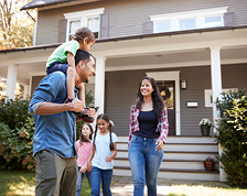 A family with a mother, father and three small children gather outside the front porch of a home