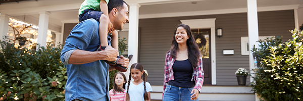 A family with a mother, father and three small children gather outside the front porch of a home