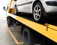 A yellow flatbed tow truck hauls a silver vehicle.