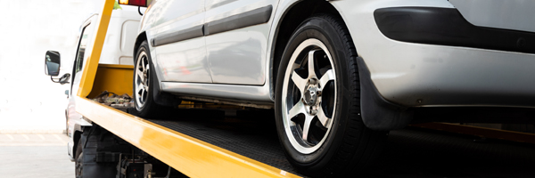 A yellow flatbed tow truck hauls a silver vehicle.