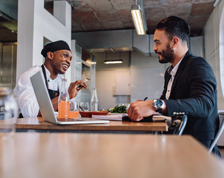 A man wearing an apron and a man wearing a business suit have a meeting in a restaurant.