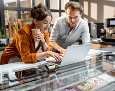 Woman in orange shirt and man in grey button down collaborate in front of a laptop computer.