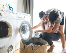Two women embrace next to clothes dryer at home