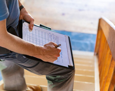 Inspector writes a note on his checklist while inspecting a home’s wooden deck