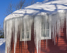 Red building with snow covered roof and long icicles hanging from its gutters