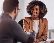 Woman wearing a blazer smiles and shakes hands with a man sitting across the table.