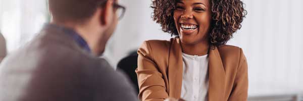 Woman wearing a blazer smiles and shakes hands with a man sitting across the table.