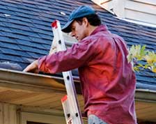 Man uses an extension ladder to clean leaves out of gutter