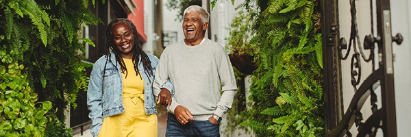A woman and man walk arm-in-arm down a path surrounded by fern plants.