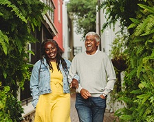 A woman and man walk arm-in-arm down a path surrounded by fern plants.