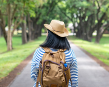 Backpacker wearing a cowboy hat walks down a tree-lined road