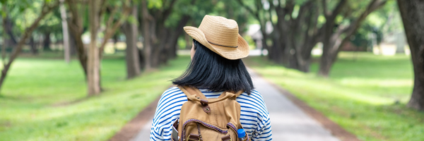 Backpacker wearing a cowboy hat walks down a tree-lined road