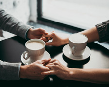 Two people hold hands next to coffee cups at a cafe