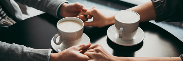 Two people hold hands next to coffee cups at a cafe