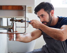 Man works on plumbing system under a bathroom sink.