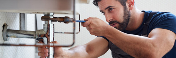 Man works on plumbing system under a bathroom sink.