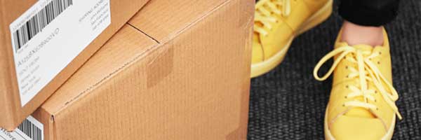 Packages stacked on porch next to woman in yellow shoes