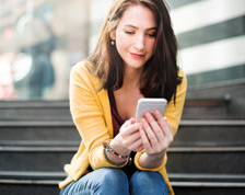 Young woman sits on stairs outside and checks her cell phone