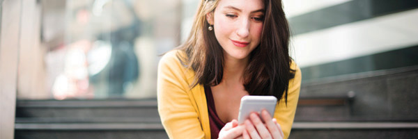 Young woman sits on stairs outside and checks her cell phone