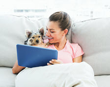 Smiling woman reads tablet on couch with her dog