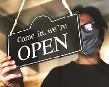 Man wearing face mask hangs open sign on store window