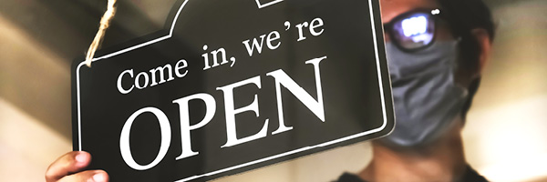 Man wearing face mask hangs open sign on store window