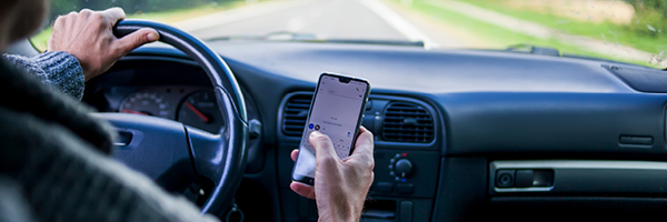 A driver steers a vehicle with their left hand while texting with their right.
