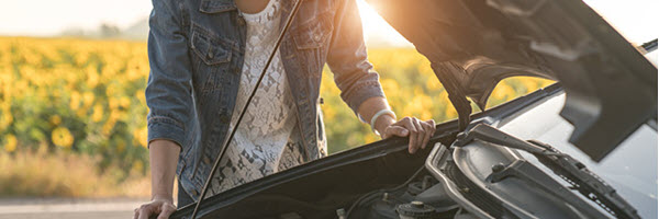 Woman experiences car trouble next to field of sunflowers