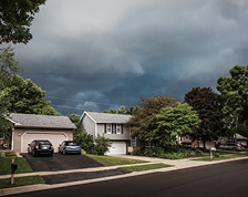 A quaint neighborhood street with large storm clouds overhead.
