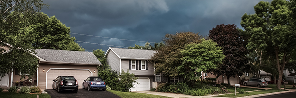 A quaint neighborhood street with large storm clouds overhead.