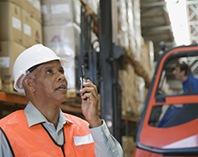 Man in safety vest and hard hat talks on walkie-talkie
