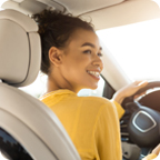 Young woman in a yellow shirt smiles while driving her car