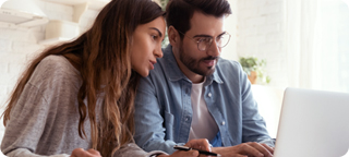 Couple sits side by side while reviewing information on a laptop computer