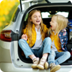 Sisters laugh while sitting in the open trunk of an SUV