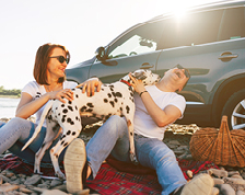 man and woman with dog having a picnic in front of car
