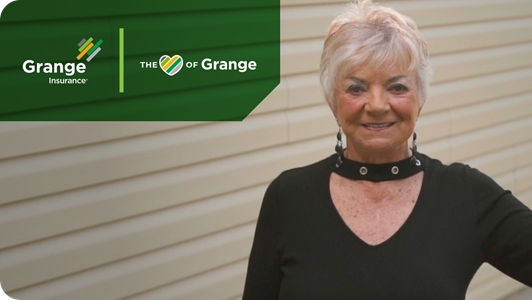 A senior woman stands in front of her home and smiles at the camera.