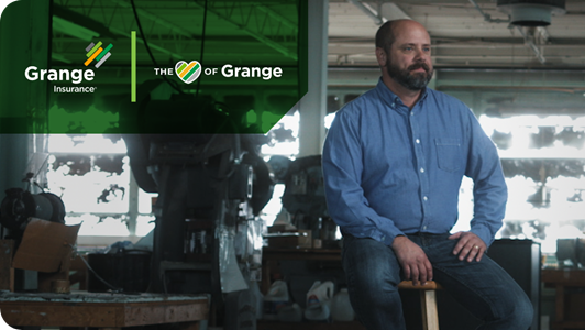 A business owner sits on a stool in a workshop. 