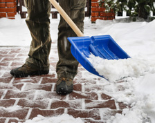 A person shovels snow off a brick path with a blue shovel.