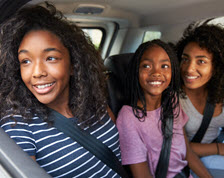 Kids in back seat smiling out the window of moving car