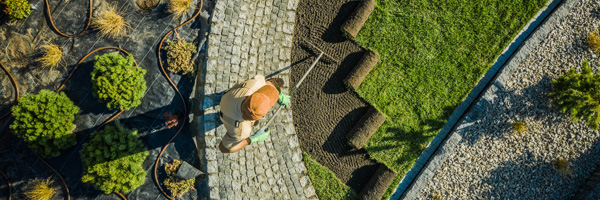 An aerial view of a landscaper tending to soil next to rolled sod and a variety of planted shrubs.