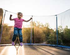 Young girl bounces in the air over a trampoline in her backyard